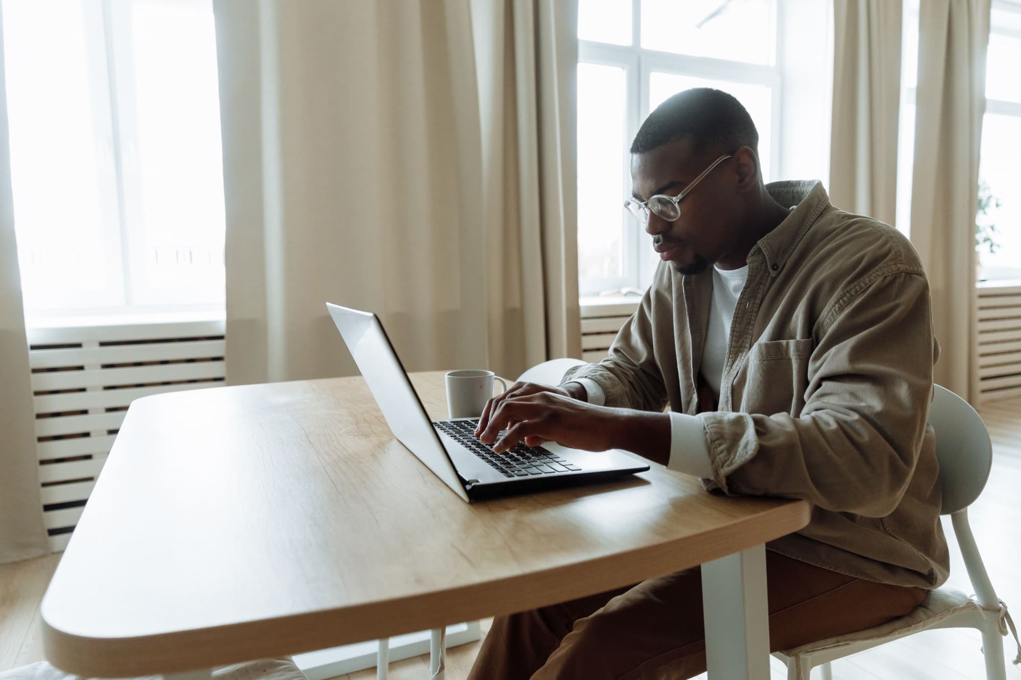 A man working on his laptop at a table by a window