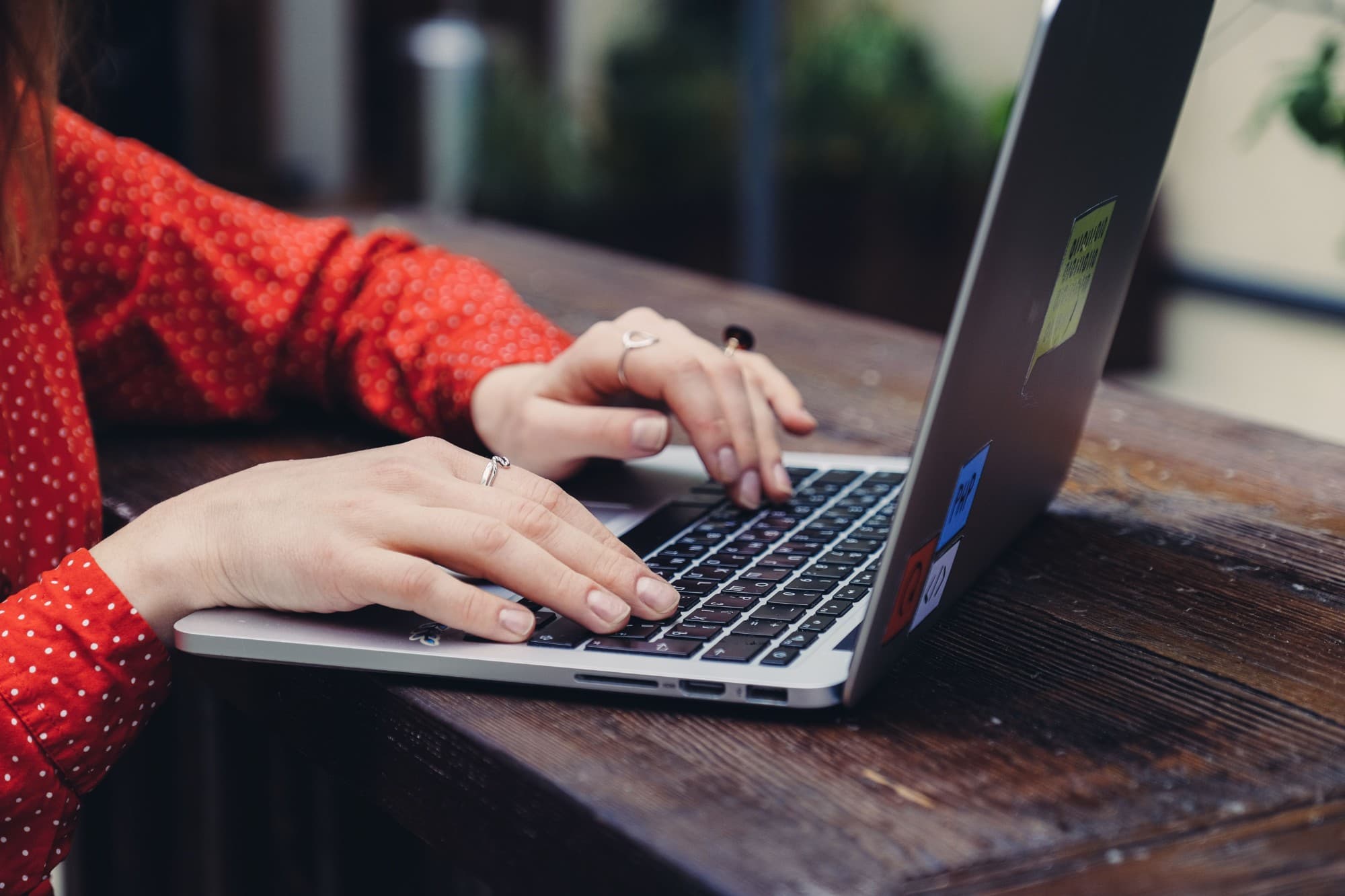 Une personne tape sur le clavier d’un ordinateur portable, posé sur une table en bois